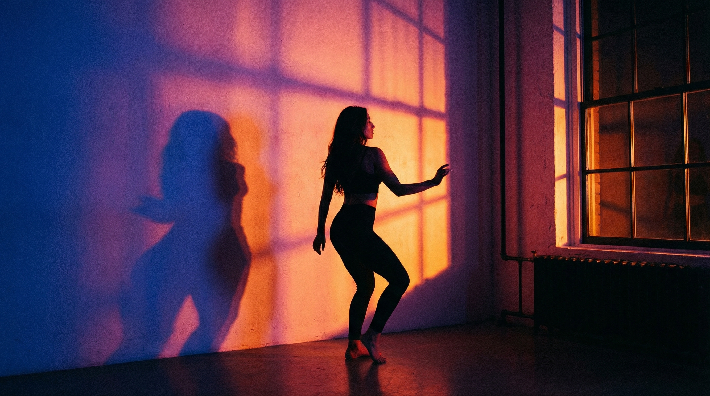 Silhouette d'une femme dansant sensuellement devant une lumière tamisée, créant un jeu d'ombres sur le mur.